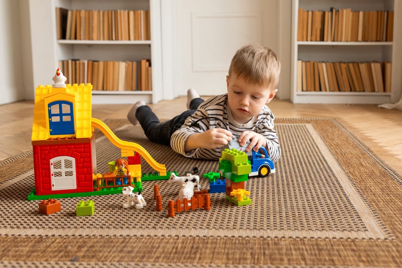 team-04 Young boy engaged in imaginative block play on a carpeted floor indoors.