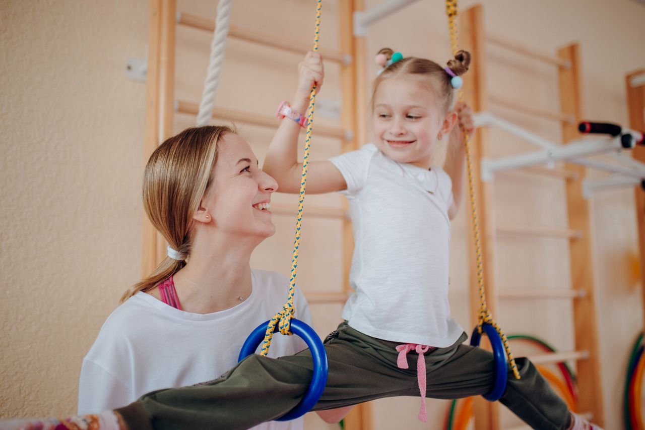 Crafting Captivating Headlines: Your awesome post title goes here Smiling mother teaches her daughter gymnastics on rings indoors, fostering bonding and flexibility.