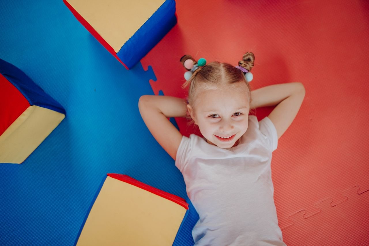 team-01 Smiling child lying on a vibrant play mat, showcasing joy and innocence in an indoor setting.
