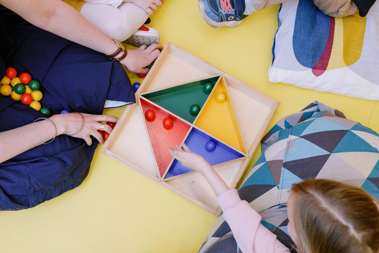 team-02 Children playing with a vibrant geometric puzzle on a yellow floor.